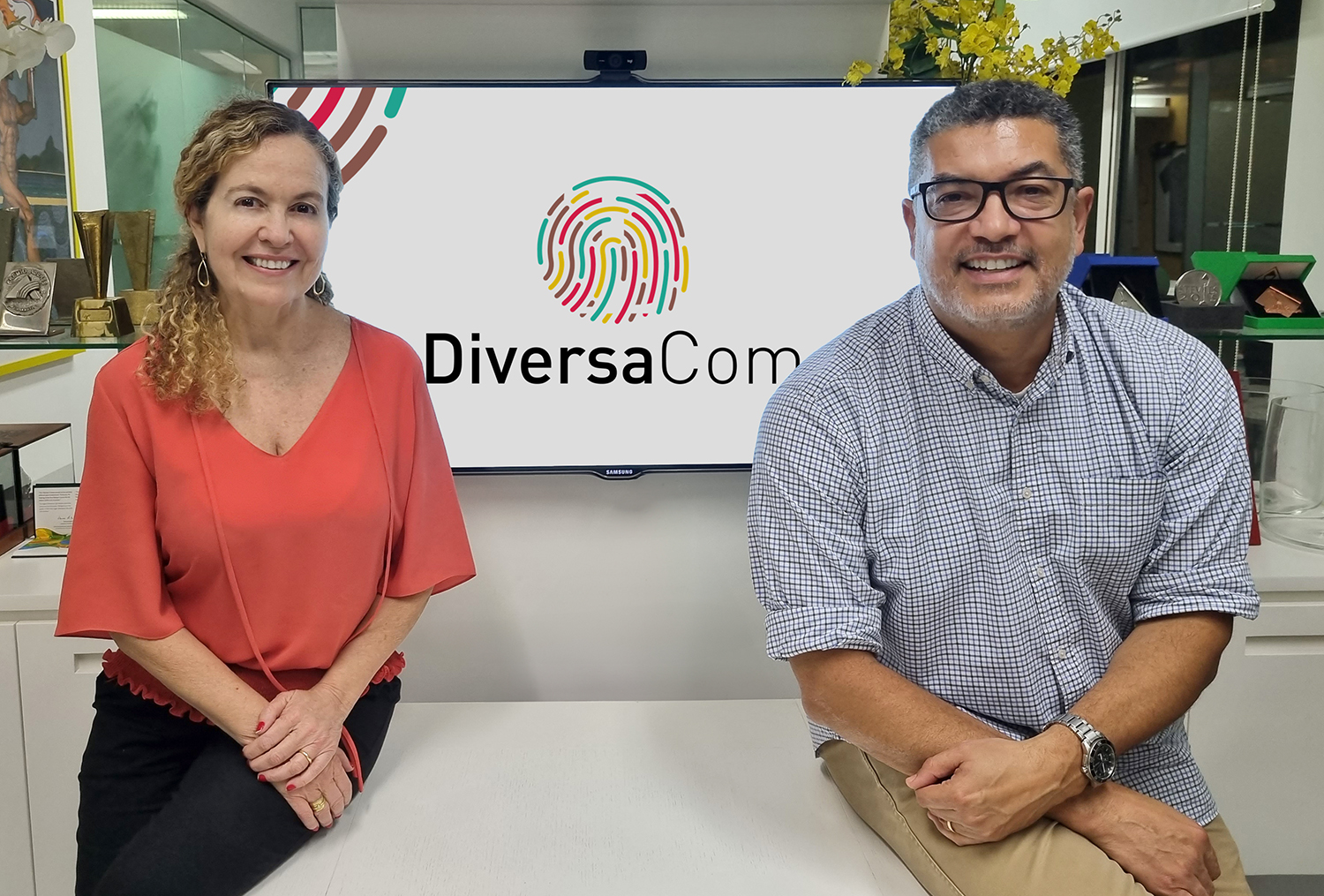 Marcelo Moreira e Carina Almeida, olhando para frente, ao meio deles está a logomarca da DiversaCom